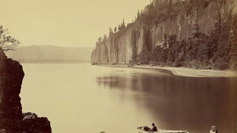 Sepia-toned calm river bordered by rocky cliffs and trees, soft warm browns and muted greens.
